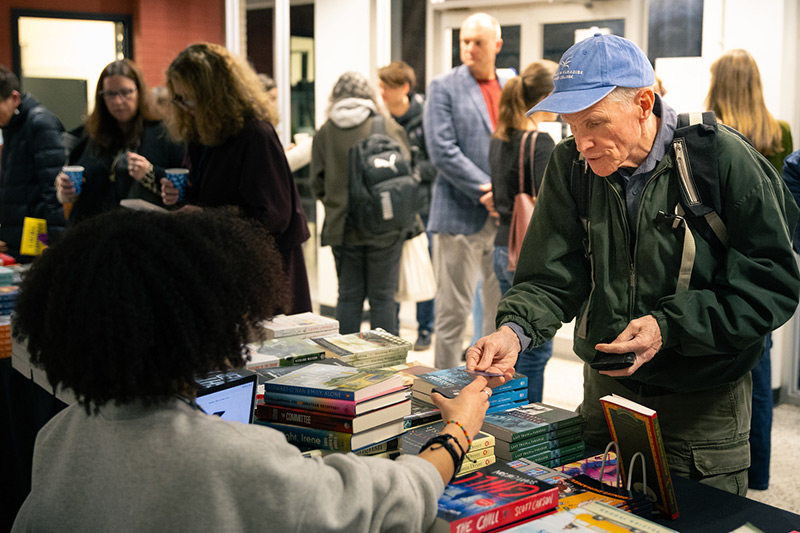 Older man in hat giving money to another person for stack of books