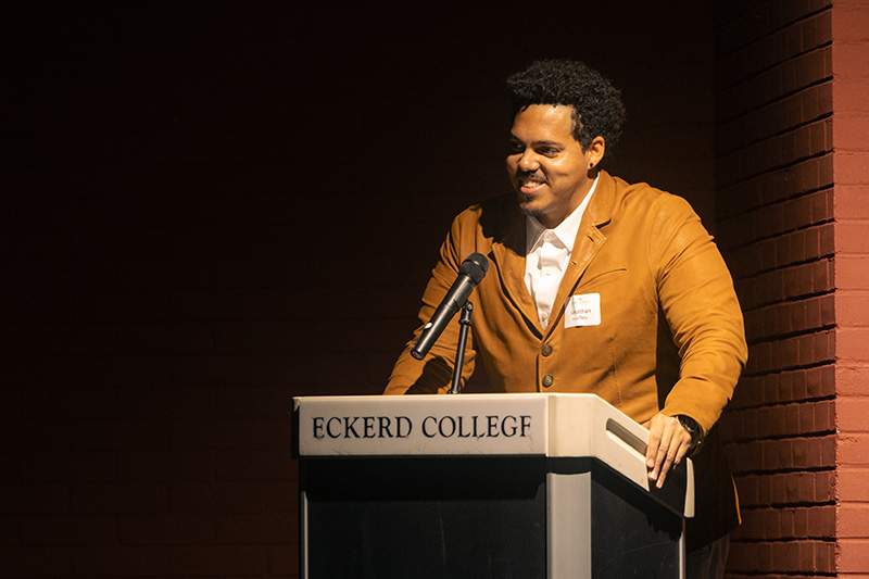 Young poet smiles as he stands at a podium that reads "Eckerd College"
